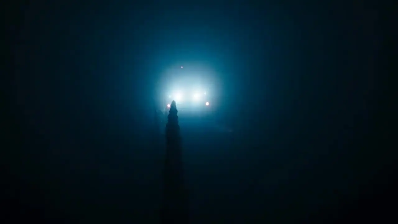 Headlights cutting through heavy fog in near-total darkness